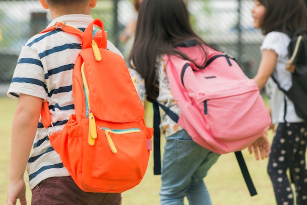 Three pupils of primary school go hand in hand. boy and girl with school bags behind the back. beginning of school lessons. warm day of fall. back to school. little first graders. Free Photo