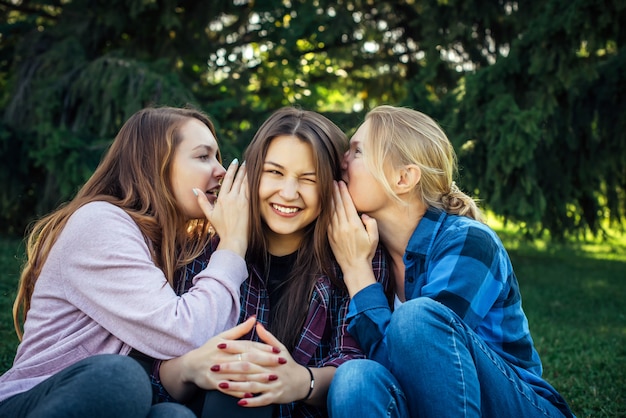 Premium Photo Three Young Attractive Woman Sharing Secrets Sitting On Green Grass In The Park