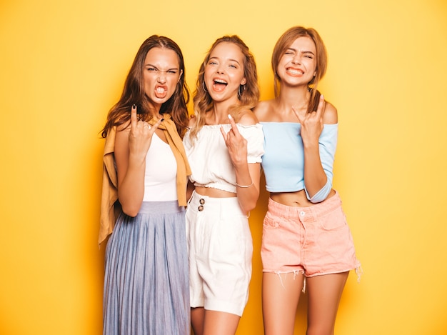 無料の写真 トレンディな夏服で3人の若い美しい笑顔流行に敏感な女の子 黄色の壁に近いポーズ セクシーな屈託のない女性 クレイジーになって楽しんでいるポジティブなモデルロックンロールの兆候を示しています