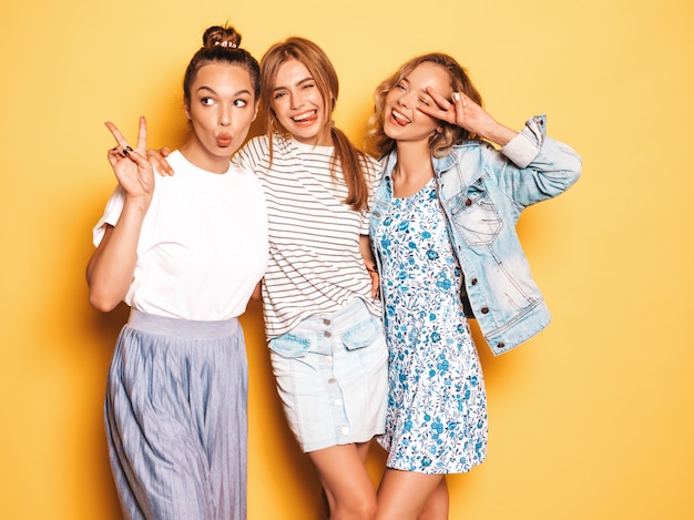 トレンディな夏服で3人の若い美しい笑顔流行に敏感な女の子 黄色の壁に近いポーズセクシーな屈託のない女性 楽しいポジティブモデル 無料の写真