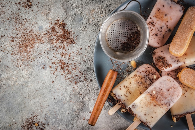 Tiramisu popsicles ice cream. gelato pops with italian savoiardi cookies, mascarpone, milk chocolate, with tiramisu ingredients on grey stone kitchen table. top view copy space Premium Photo