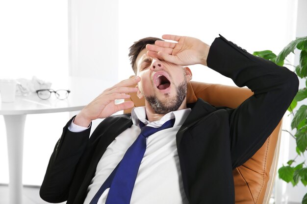 Premium Photo | Tired business man yawning and stretching at workplace ...