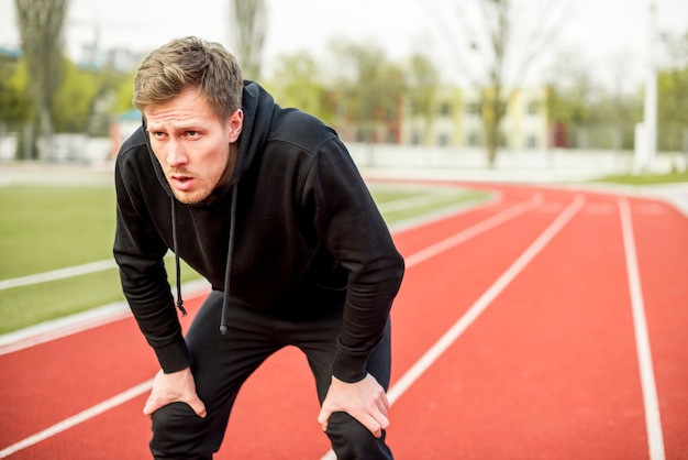 Tired male athlete standing on race track Photo | Free Download