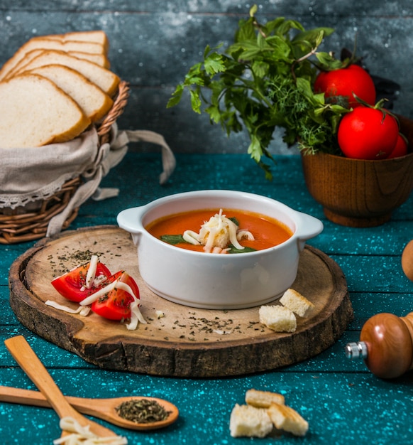 Tomato soup with parmesan on a piece of woode with tomatoes and crackers around. Free Photo