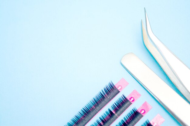 Tools for eyelash extension procedure. two tweezers with artificial black lashes on blue background. Premium Photo