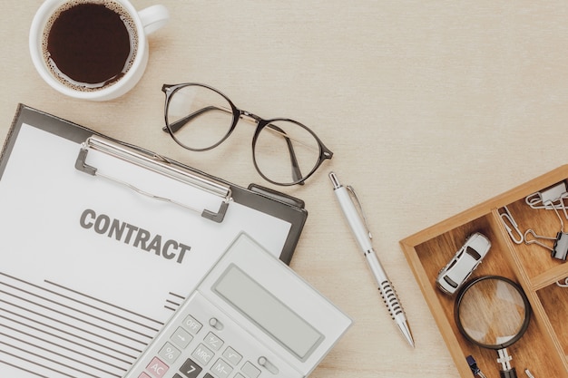 Top view business contract form with coffee eyeglasses car calculator pen with magnifying glass on wooden background. Free Photo