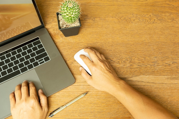 Top view of business man hand using laptop and holding mouse with pen on wooden desk. Premium Photo