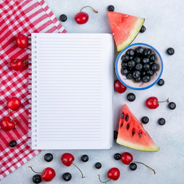 Free Photo Top View Copy Space Notebook With Slices Of Watermelon With Cherries And Blueberries In A Cup