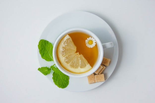 Top view a cup of chamomile tea with lemon, mint leaves, sugar on white surface. horizontal Free Photo