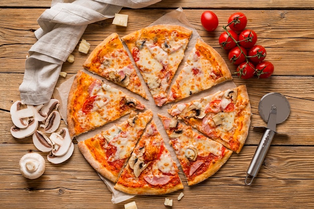 Top view of delicious pizza on wooden table with tomatoes and cheese around it