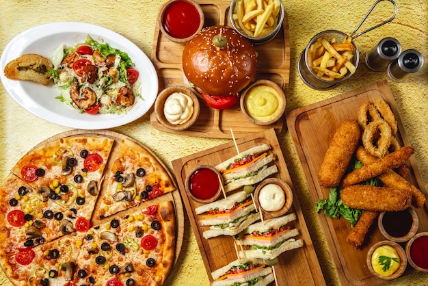 Free Photo | Top view fast food mix mozzarella sticks club sandwich  hamburger mushroom pizza caesar shrimp salad french fries ketchup mayo and  cheese sauces on the table
