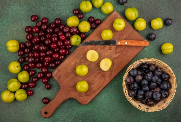 Top View Of Fresh Green Cherry Plums On A Wooden Kitchen Board With Knife With Red Cherries With Sloes On A Bucket On A Green Background Free Picture On Freepik