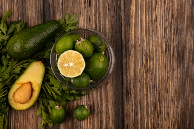 Top view of green skinned feijoas with limes on a glass bowl with avocado feijoas and parsley isolated on a wooden surface with copy space Free Photo