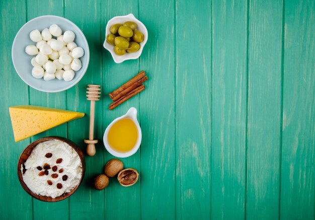 Download Free Photo Top View Of Mozzarella Cheese In A Bowl Cottage Cheese And A Piece Of Dutch Cheese With Walnuts Honey Cinnamon Sticks And Pickled Olives On Green Wood With Copy