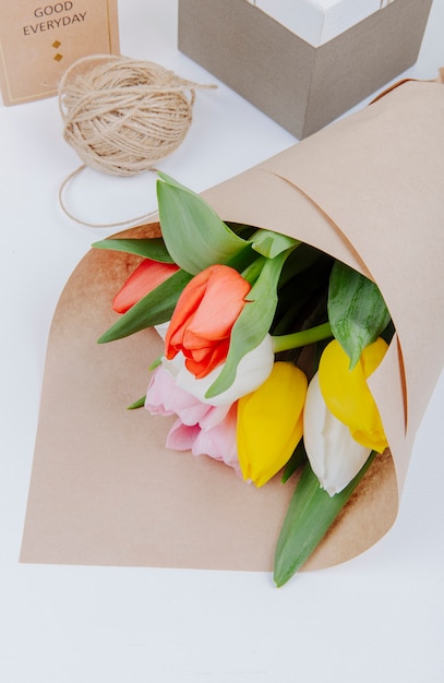白い背景の上のギフトボックスとロープのペーパークラフトでカラフルなチューリップの花の花束のトップビュー 無料の写真