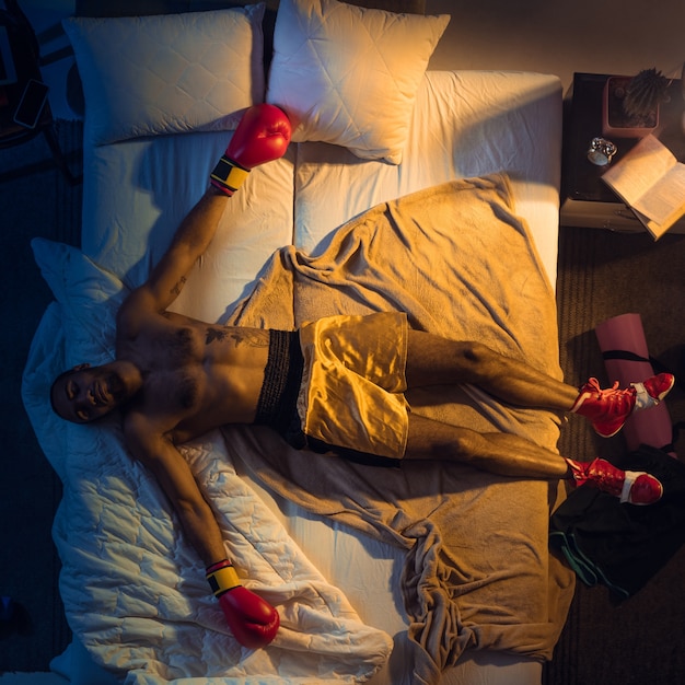 若いプロのボクサー 手袋をはめてスポーツウェアで彼の寝室で寝ている戦闘機の上面図 無料の写真