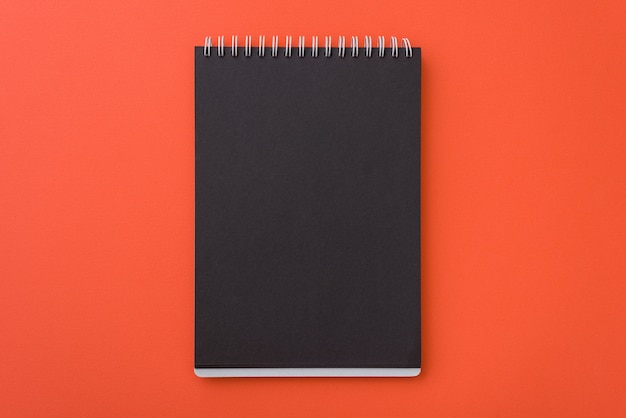 Top view of open spiral blank black notebook l on orange desk background, place for your text Premium Photo
