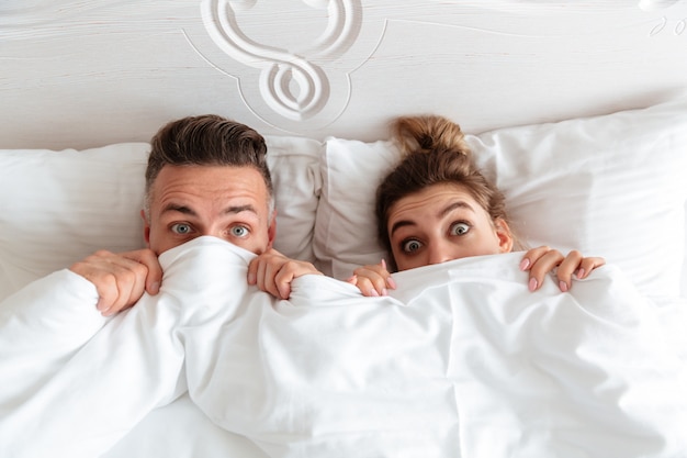 Top View Of Shocked Lovely Couple Lying Together In Bed