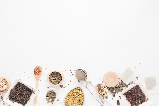 Top view of variety of herbs; spoon; tea strainer; dry tea leaves arranged on white background Free Photo
