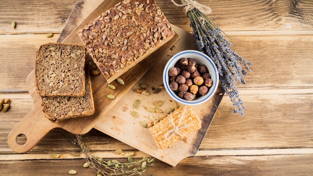 Top view of whole grain bread and hazelnut in bowl with protein bar on chopping board Free Photo