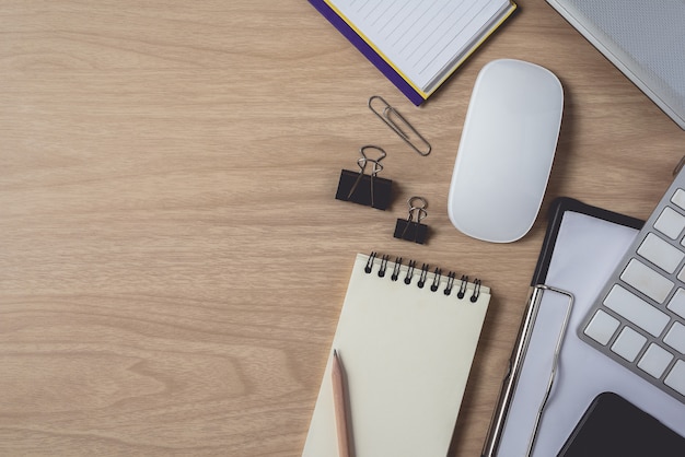 Top view of workspace with diary or notebook and clipboard, laptop, mouse computer, keyboard, smart phone, pencil, pen on wooden background Premium Photo