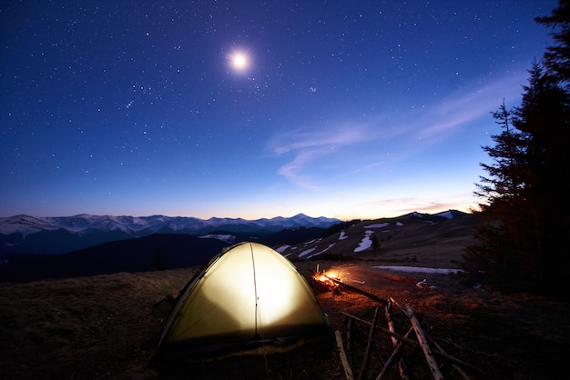Premium Photo Tourist Camping Near Forest In The Mountains Illuminated Tent And Campfire Under Evening Sky Full Of Stars And The Moon