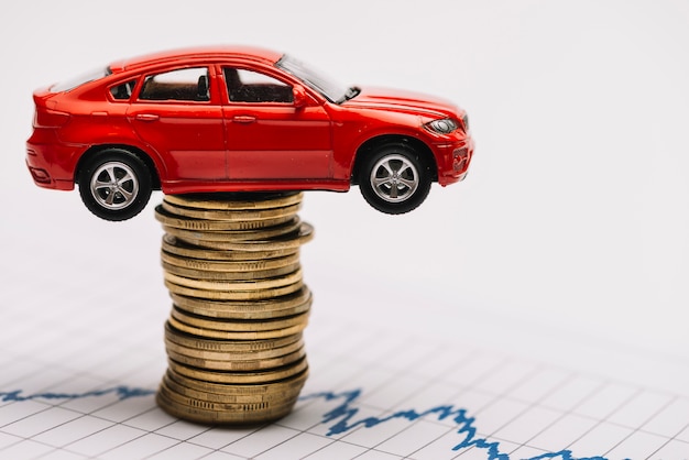 Toy red car on the stack of golden coins over the stock market graph Free Photo