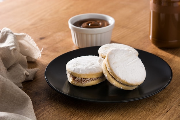 Traditional argentinian alfajores with dulce de leche and sugar on wooden table Premium Photo