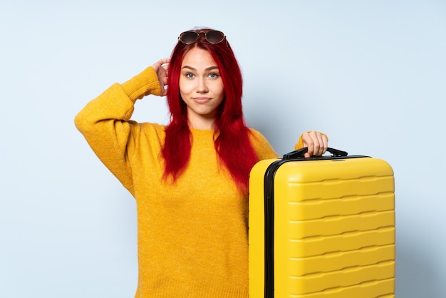 Traveler girl holding a suitcase isolated on blue having doubts ...