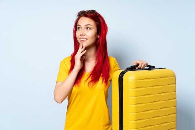 Traveler girl holding a suitcase isolated on blue looking up while ...