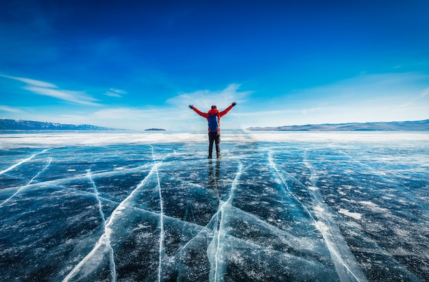 旅行者の男性は赤い服を着て ロシアのシベリアのバイカル湖で凍った水の自然な砕氷の上に立って腕を上げています プレミアム写真