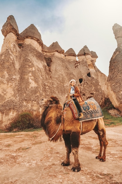 カッパドキア ギョレメの妖精の煙突でラクダに乗っている旅行者の女性 プレミアム写真