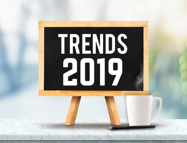 Trends 2019 on blackboard with easel on marble table with sun and blur green tree bokeh ba Premium Photo