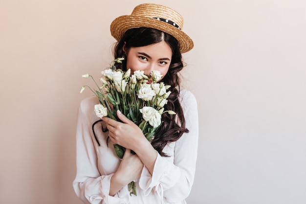 花を嗅ぐトレンディなアジアの女性 白いトルコギキョウの花束を保持しているロマンチックなブルネットの若い女性 無料の写真