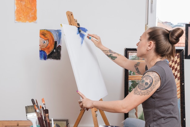 Trendy young woman with tattoos painting in blue Free Photo