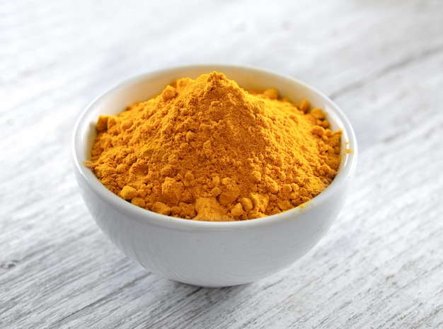 Premium Photo | Turmeric powder in white cup on wooden floor