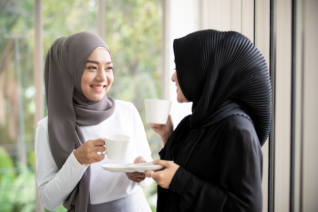 Two asian muslim woman standing and talking in the office with a ...
