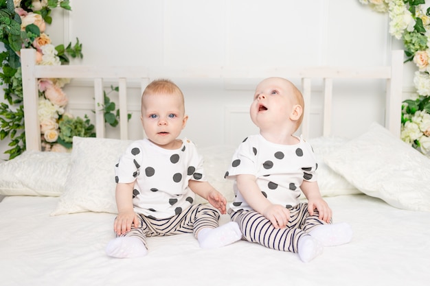 同じ服を着てベッドに座っている8ヶ月の双子の赤ちゃん2人 兄弟姉妹関係 双子の子供のためのおしゃれな服 プレミアム写真