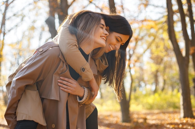 두 명의 아름다운 여자 친구가 함께 시간을 보내고 있습니다 가 공원에서 산책 하 고 포옹 두 젊은 웃는 자매 코트를 입고