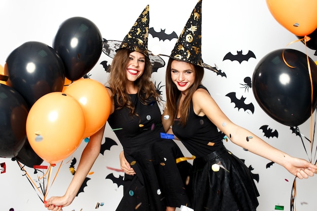 Premium Photo Two Beautiful Girls In Black Dresses And Witch Hats Have Fun With Black And 4803