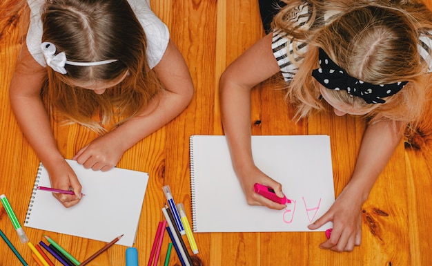 Premium Photo Two Caucasian Girls Having Fun On The Floor Drawing And Writing Overhead 2540