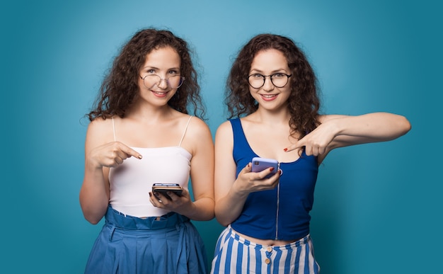 Premium Photo Two Caucasian Sisters Pointing At The Phone While Wear
