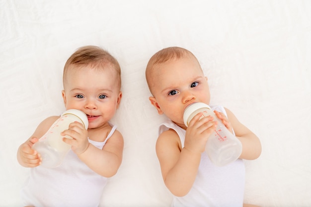 Premium Photo Two Children A Boy And A Girl Twins Of 8 Months Drink Milk From A Bottle On The Bed In The Nursery Feeding The Baby Baby Food Concept Top View