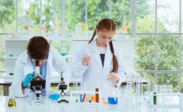 Two children scientists making experiments chemical with looking microscope in the laboratory room. Premium Photo
