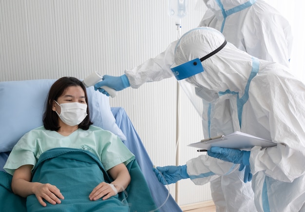 Premium Photo | Two doctor wear ppe suit with face mask, measure body  temperature of coronavirus infected patient with infrared thermometer gun  in negative pressure quarantine room.