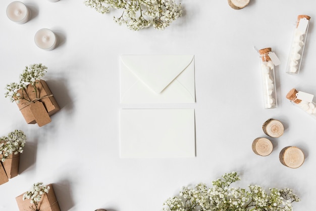 Two envelope surrounded with baby's-breath flowers; candles; marshmallow test tubes; miniature tree stumps and gift boxes on white background Free Photo