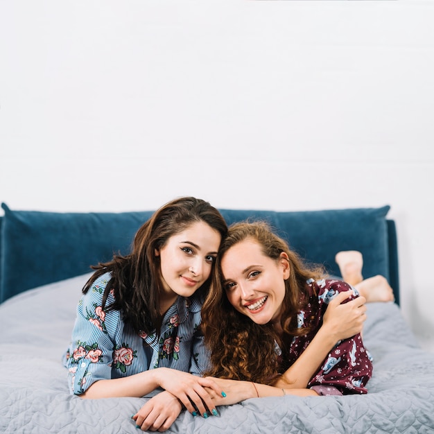 Two female friends lying on bed looking at camera Free Photo