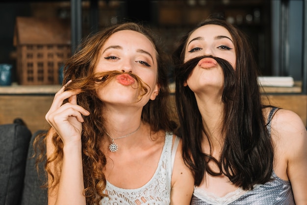 Two female friends making fake moustache with their hair Free Photo