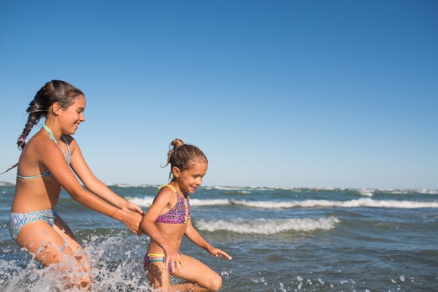 2人の面白い女の子が騒々しい海の波に飛び乗って 晴れた暖かい夏の日に待望の休暇を楽しんでいます プレミアム写真