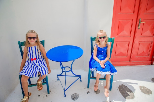 Premium Photo Two Girls In Blue Dresses Sitting In Outdoor Cafe On Street Of Typical Greek Village On Mykonos Island Greece